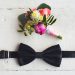 Close up of man accessories. Black bowtie and flower boutonniere on white wood rustic background. Set for formal style of wearing isolated on white wooden background.