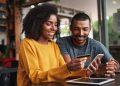 Young african man looking at his girlfriend using credit card and smartphone for shopping online in cafe
